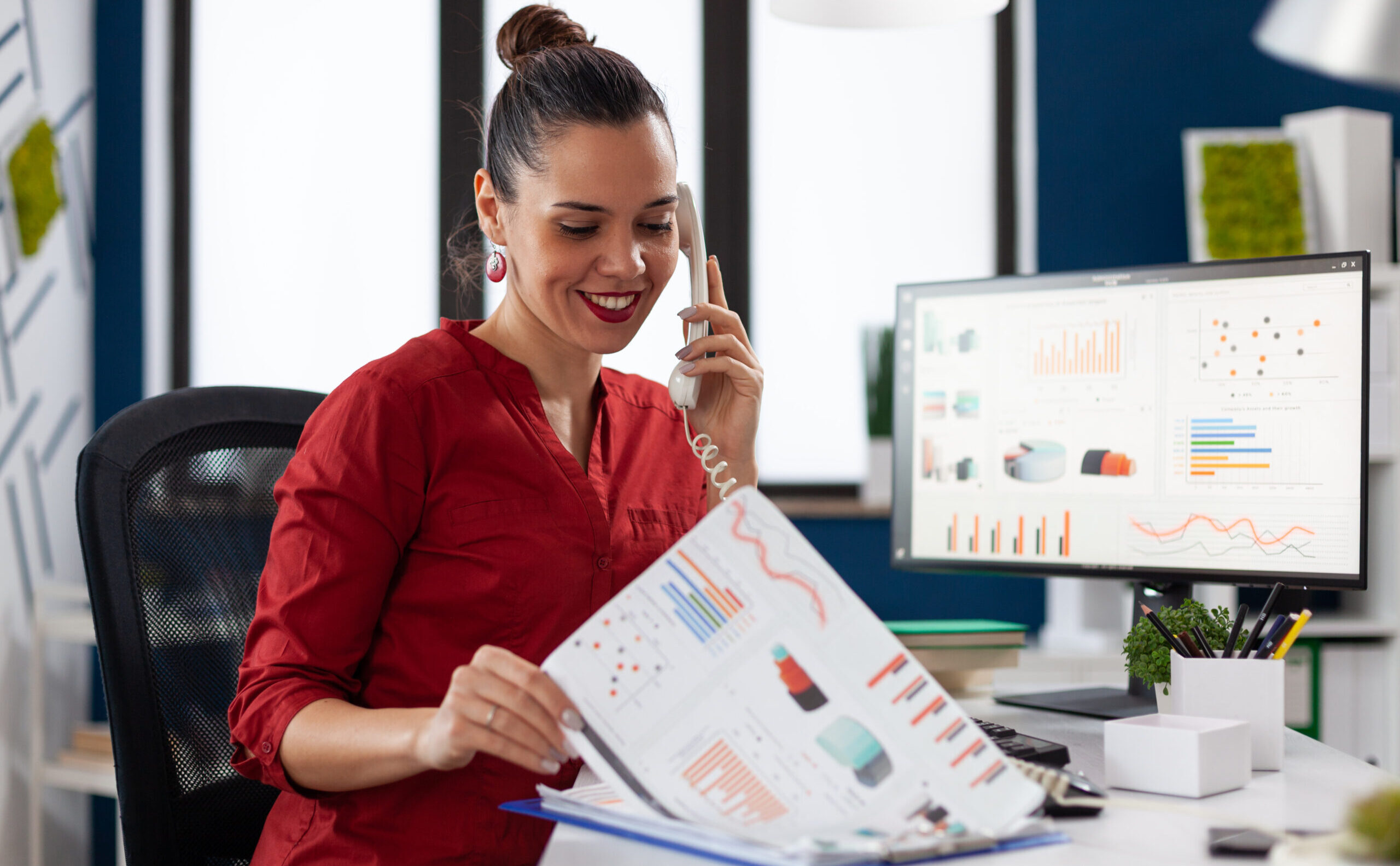 Businesswoman in company office checking finaicial statistics on clipboard, discusing details with coworkers during phone call conversation. Happy entrepreneur communicating with client.